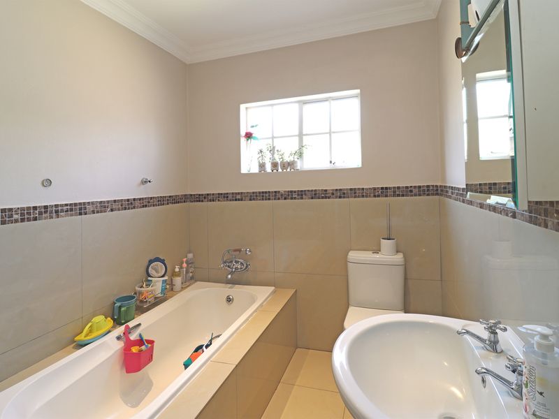 A functional bathroom featuring a built-in bathtub, pedestal washbasin, toilet, and neutral wall tiling with a decorative mosaic border.