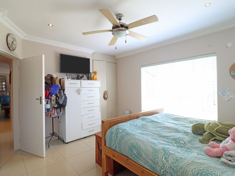 A well-maintained bedroom featuring tiled flooring, built-in cupboards, a ceiling fan, and recessed lighting, offering a comfortable and functional living space.