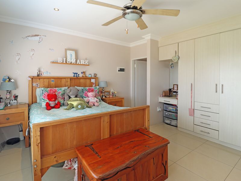 A well-maintained bedroom featuring built-in cupboards, tiled flooring, and a ceiling fan, offering a functional and comfortable living space.