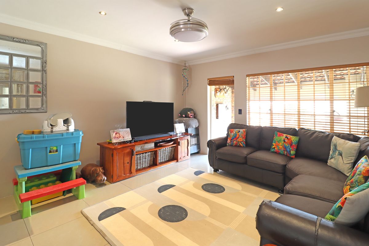 A comfortable living room featuring tiled flooring, recessed lighting, a ceiling fan, and large windows with wooden blinds allowing for natural light.