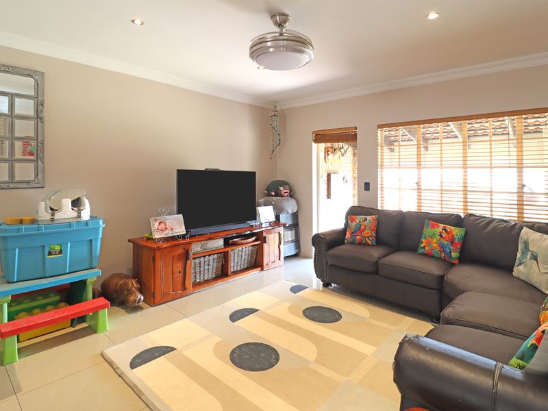 A comfortable living room featuring tiled flooring, recessed lighting, a ceiling fan, and large windows with wooden blinds allowing for natural light.