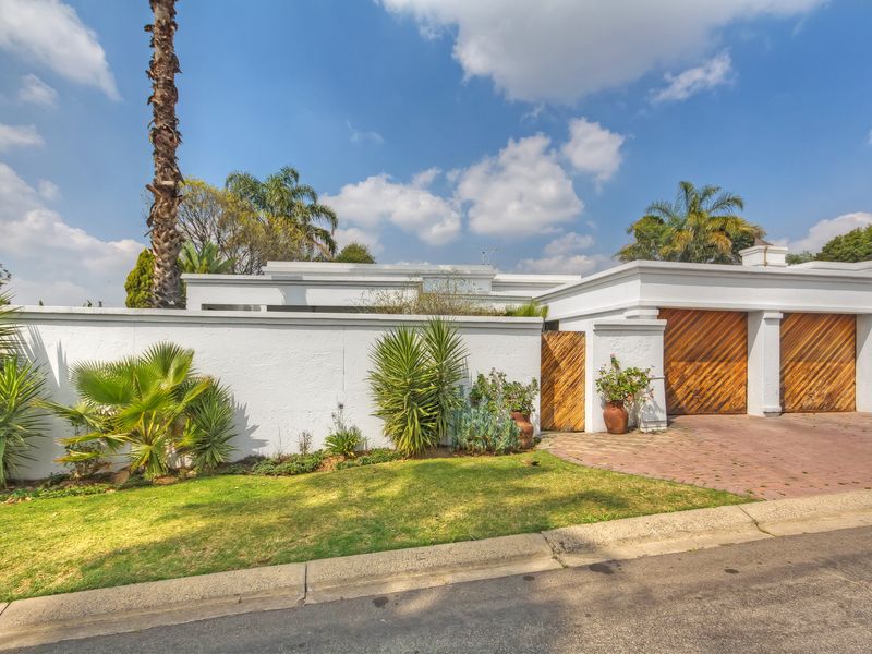 Front elevation of the townhouse featuring a paved driveway, double wooden garage doors, and a secure boundary wall with a pedestrian entrance.