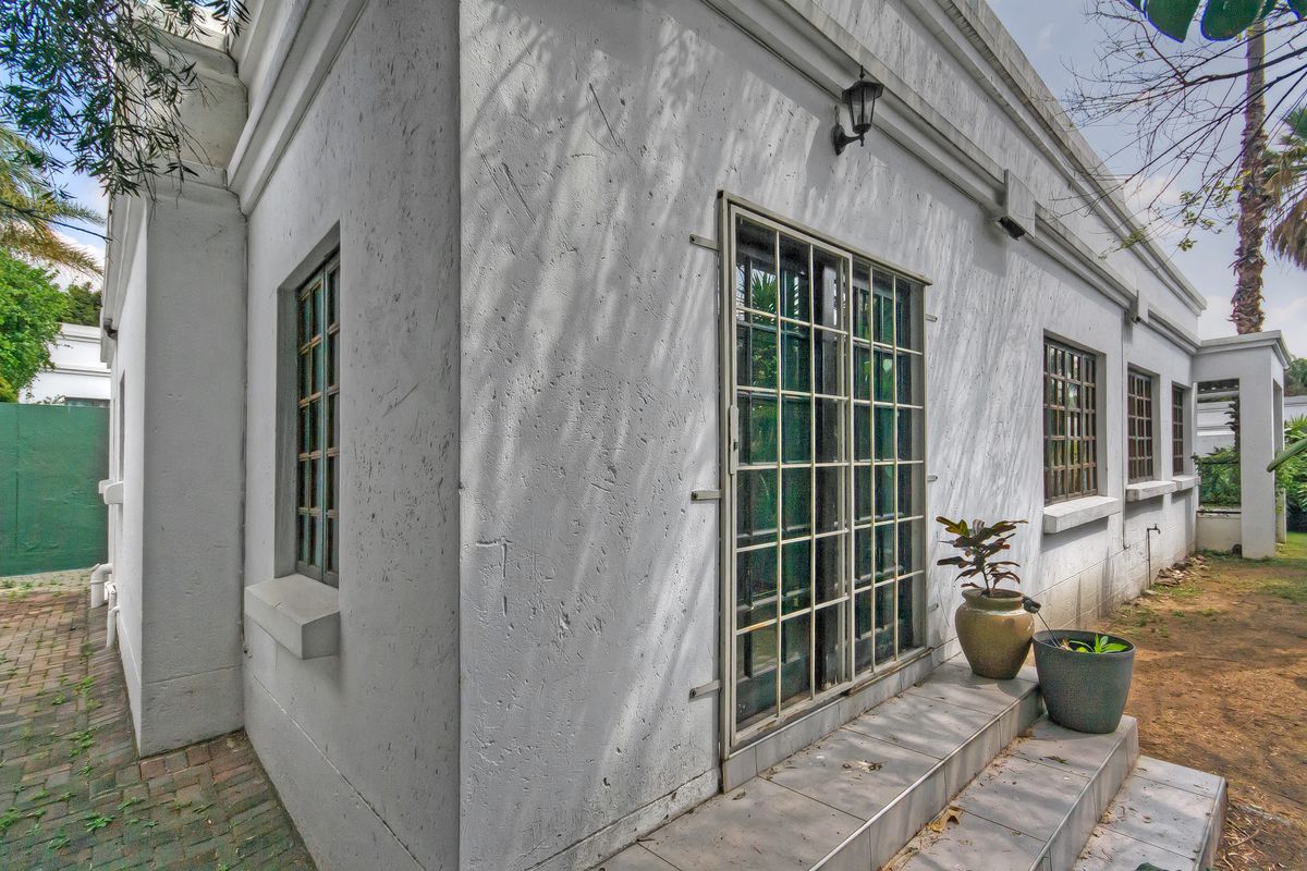 Rear exterior view of the townhouse featuring white plastered walls, security-barred windows, a tiled entrance step, and brick paved pathways.