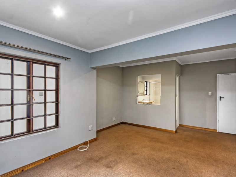 An empty bedroom featuring built-in cupboards, timber-framed windows, and an internal window looking into the adjacent bathroom area.