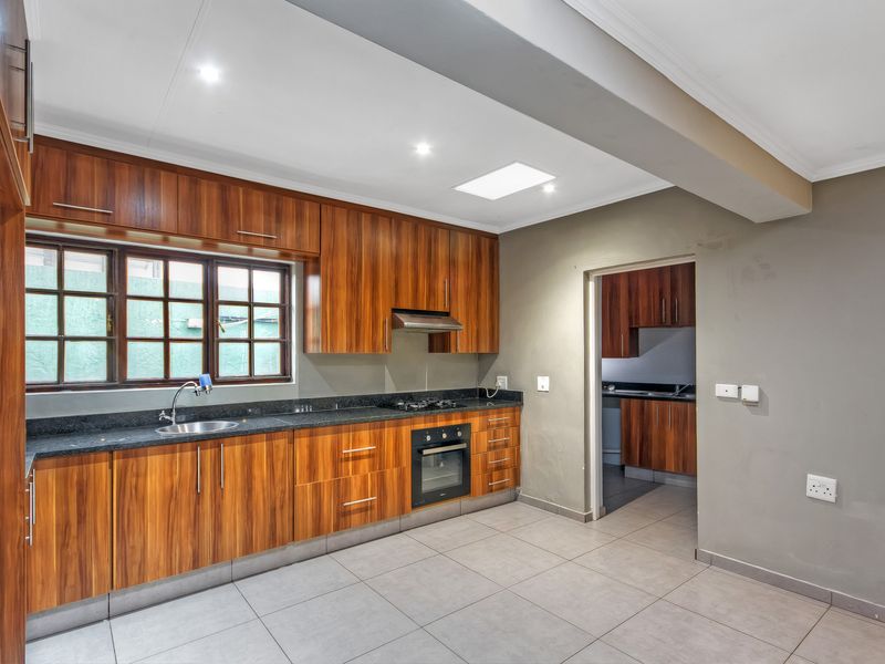 Modern kitchen featuring wood grain cabinetry, granite countertops, built-in oven, gas hob, and a convenient adjoining scullery area.