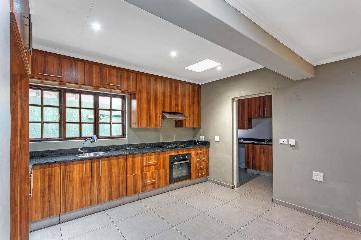 Modern kitchen featuring wood grain cabinetry, granite countertops, built-in oven, gas hob, and a convenient adjoining scullery area.