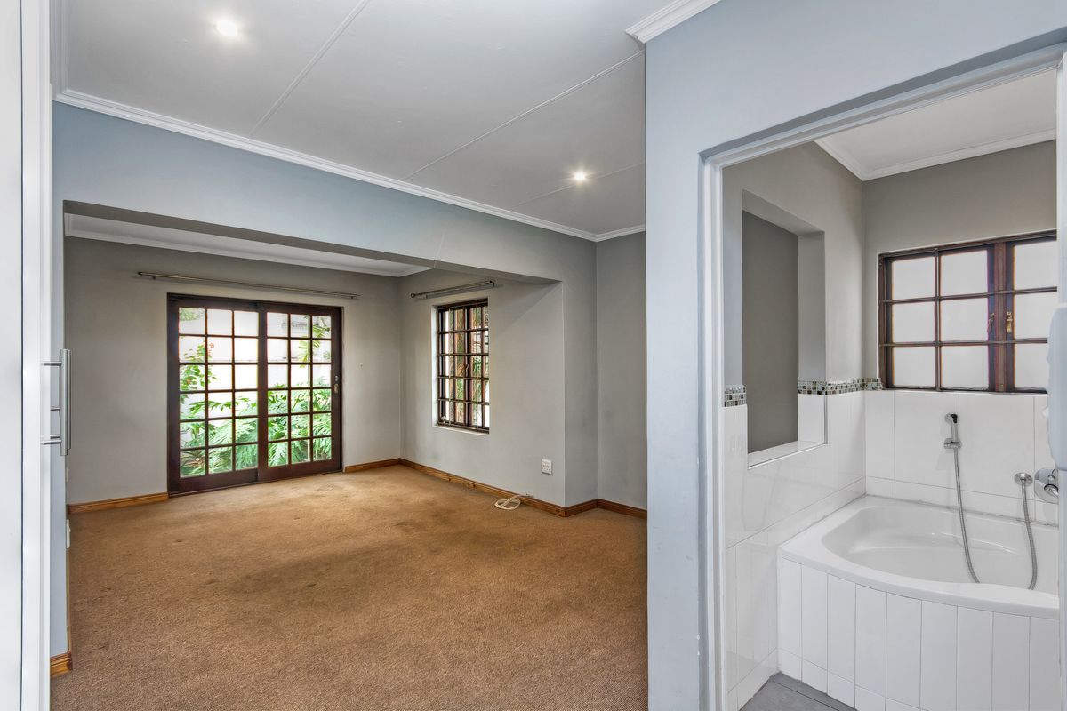 Spacious bedroom featuring neutral walls, carpeted flooring, and an en-suite bathroom with a built-in bathtub, offering direct access to the garden via sliding doors.
