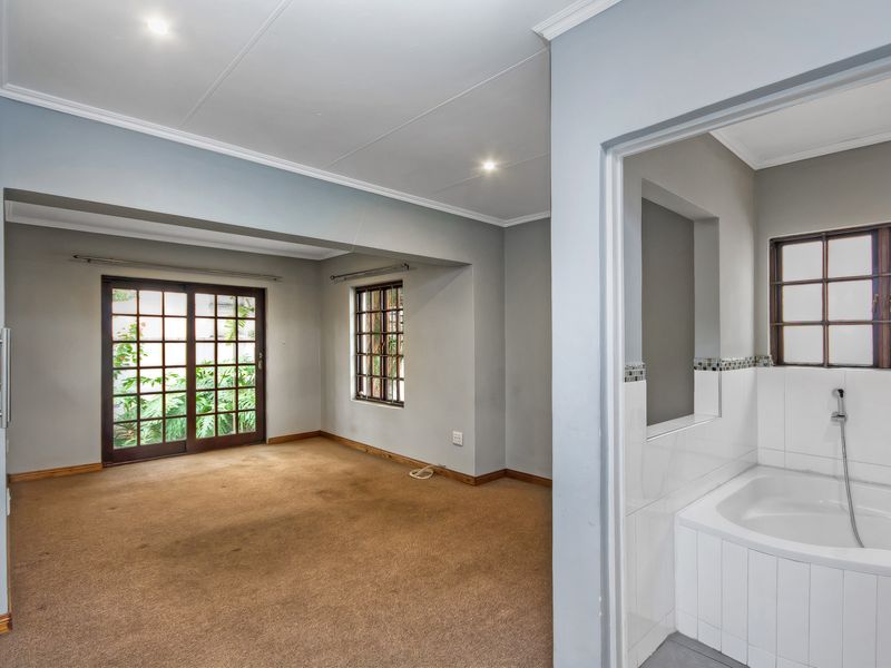 Spacious bedroom featuring neutral walls, carpeted flooring, and an en-suite bathroom with a built-in bathtub, offering direct access to the garden via sliding doors.
