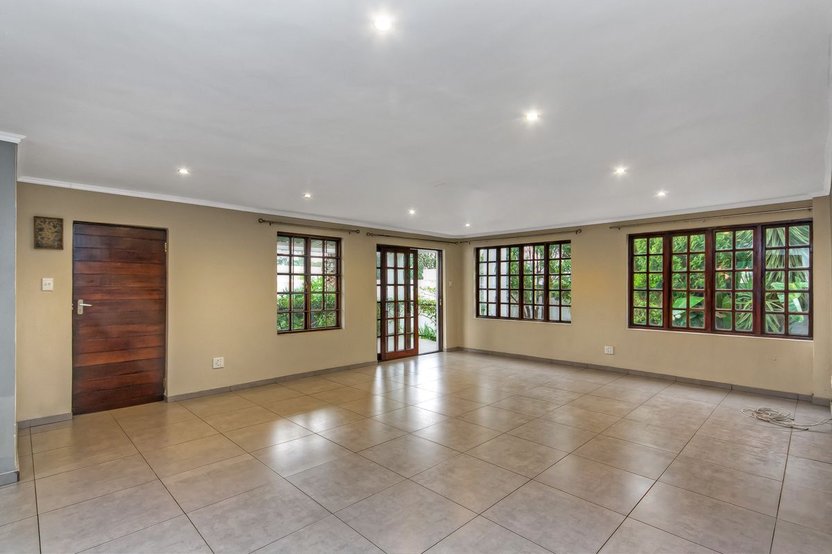 Spacious, empty living area featuring neutral tiled flooring, recessed downlights, and multiple wooden-framed windows and doors providing natural light and garden access.