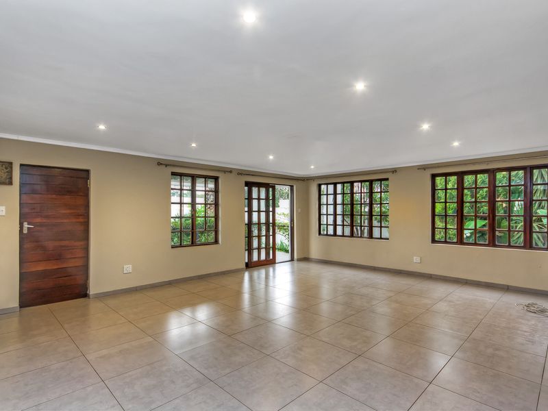 Spacious, empty living area featuring neutral tiled flooring, recessed downlights, and multiple wooden-framed windows and doors providing natural light and garden access.