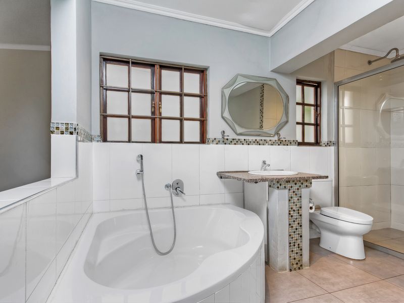 A functional bathroom featuring a corner bathtub, separate shower enclosure, pedestal vanity, and mosaic tile accents with neutral wall finishes.