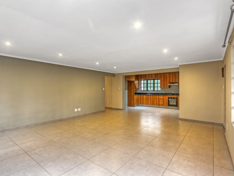 Spacious open-plan living area featuring neutral tiled floors, recessed lighting, and a functional kitchen with built-in cabinetry, oven, and hob.