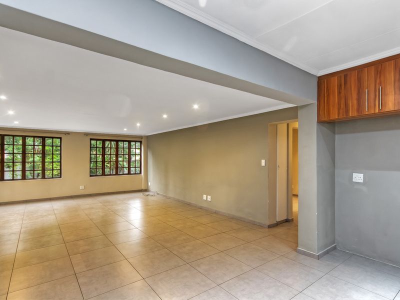 Spacious open-plan living area featuring neutral tiled flooring, recessed downlights, and large wooden-framed windows, offering a bright and versatile layout.