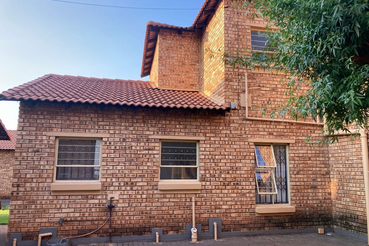 Rear elevation of a double-story face brick townhouse featuring tiled roofing, security-fitted windows, and a paved ground-level walkway.