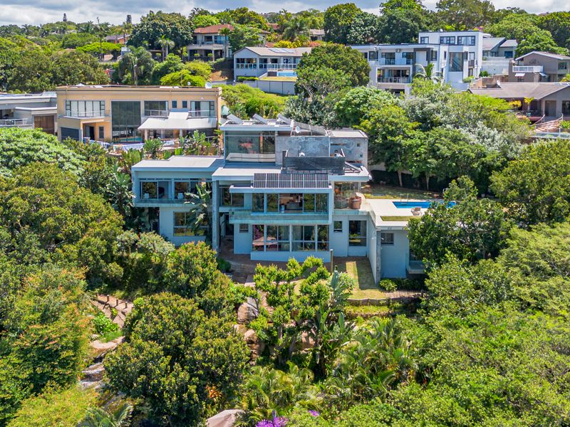 Aerial view of a modern multi-level residential property featuring a swimming pool, solar panels, and extensive surrounding greenery in a suburban setting.