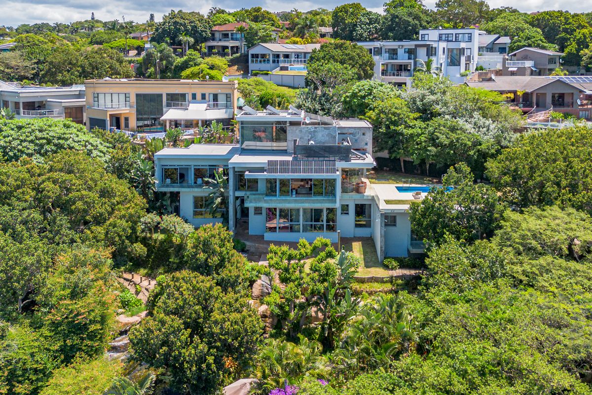Aerial view of a modern multi-level residential property featuring a swimming pool, solar panels, and extensive surrounding greenery in a suburban setting.
