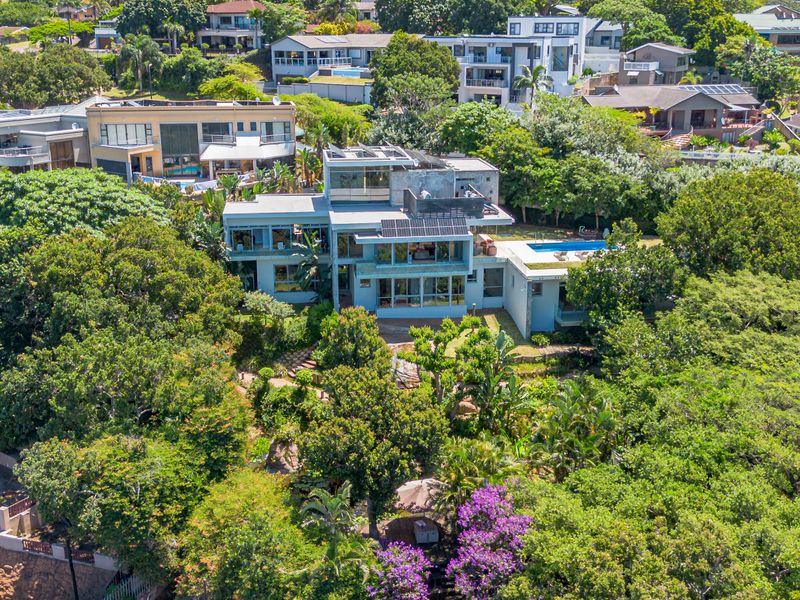 Aerial view of a multi-level modern residence featuring a swimming pool, solar panels, and extensive surrounding greenery in a residential estate.