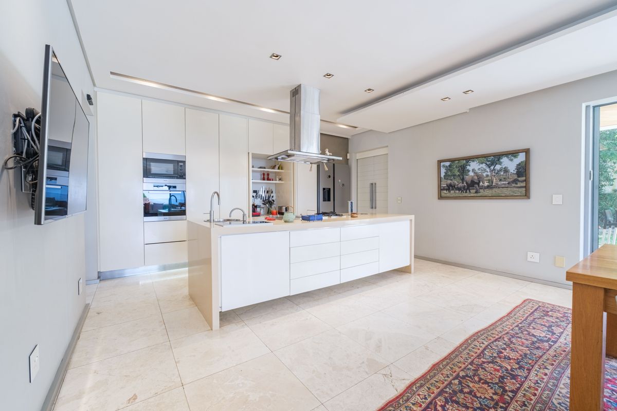 Modern, high-end kitchen featuring a central island, integrated appliances, sleek white cabinetry, and polished stone flooring with recessed lighting.