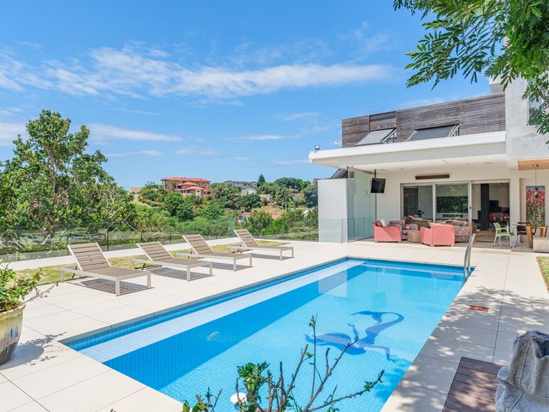 A modern outdoor pool area featuring a tiled deck, glass balustrades, and a covered patio with timber cladding, overlooking a scenic landscape.