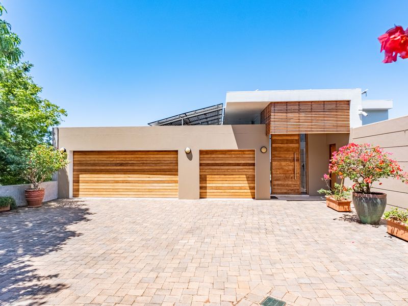 Modern front elevation featuring a double garage with timber doors, a matching timber entrance door, and integrated solar panels on the roof.