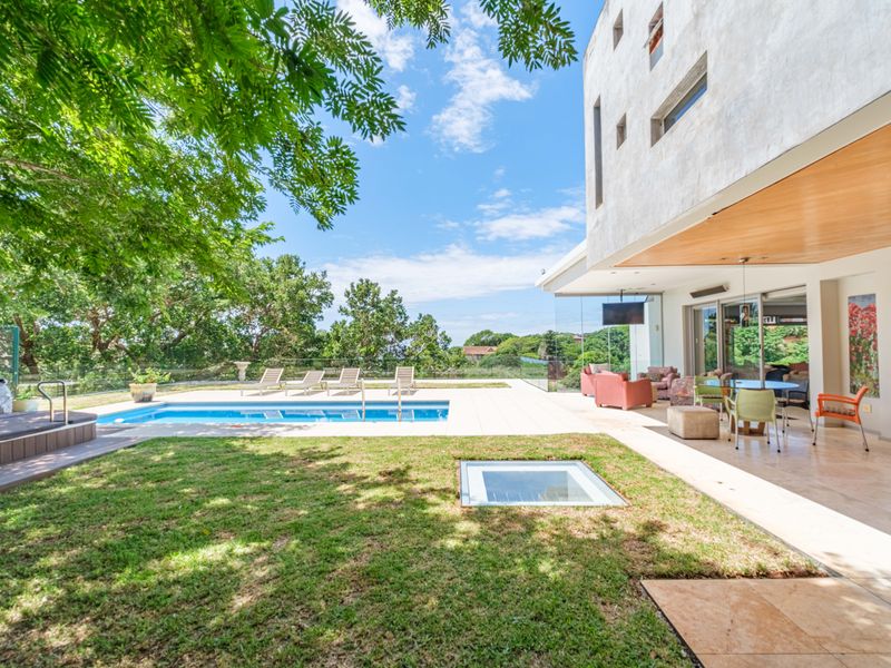 Spacious outdoor entertainment area featuring a swimming pool, covered patio with recessed lighting, and a modern glass balustrade overlooking the garden.