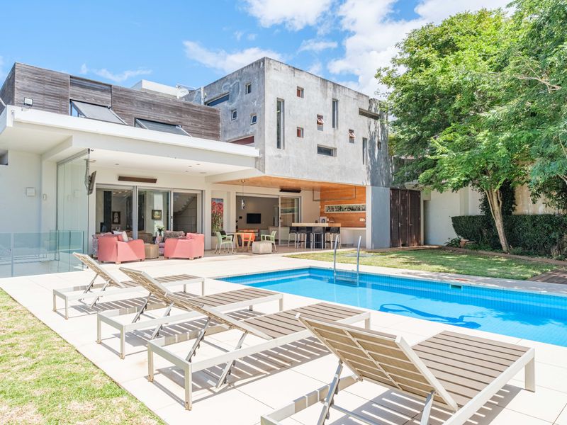 Rear exterior view featuring a modern concrete and timber home, a swimming pool, tiled deck, and a covered patio with an integrated bar area.