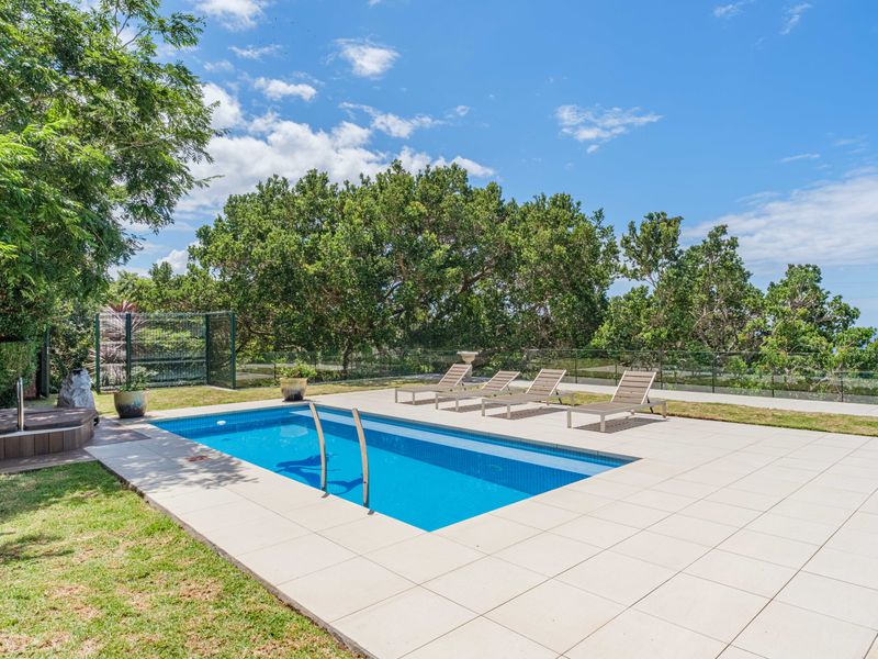 A well-maintained outdoor swimming pool area featuring a tiled deck, glass balustrade, and surrounding landscaped garden with mature trees.