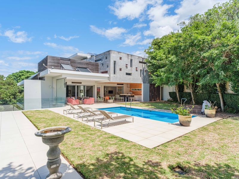 Rear exterior view of a modern multi-level home featuring a swimming pool, tiled patio area, and landscaped garden.