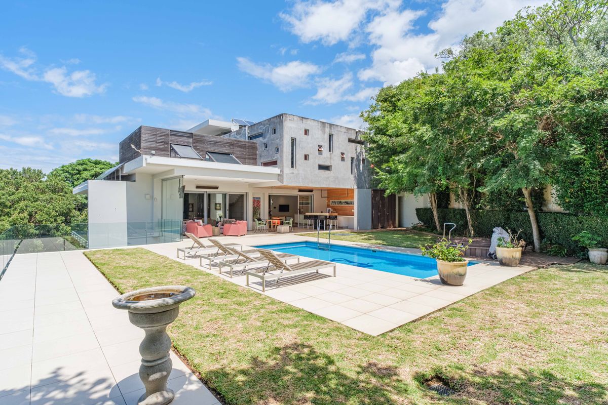 Rear exterior view of a modern multi-level home featuring a swimming pool, tiled patio area, and landscaped garden.