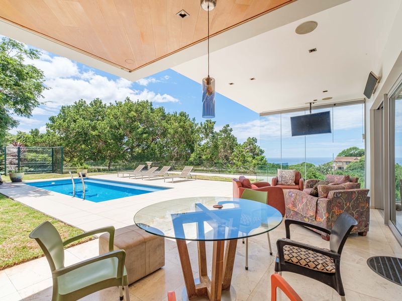 Spacious covered patio featuring stone flooring and timber ceiling, seamlessly flowing to a private swimming pool with scenic coastal views.