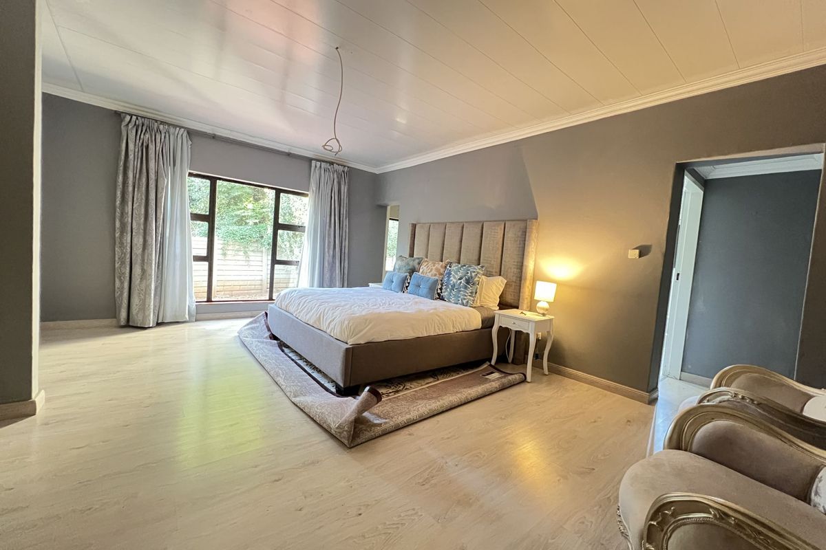 Spacious bedroom featuring light wood-look flooring, neutral grey walls, crown molding, and a large window providing natural light.