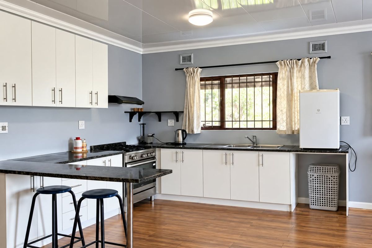 A clean, functional kitchen featuring white cabinetry, dark laminate countertops, a gas stove, and wood-look laminate flooring with a breakfast bar area.
