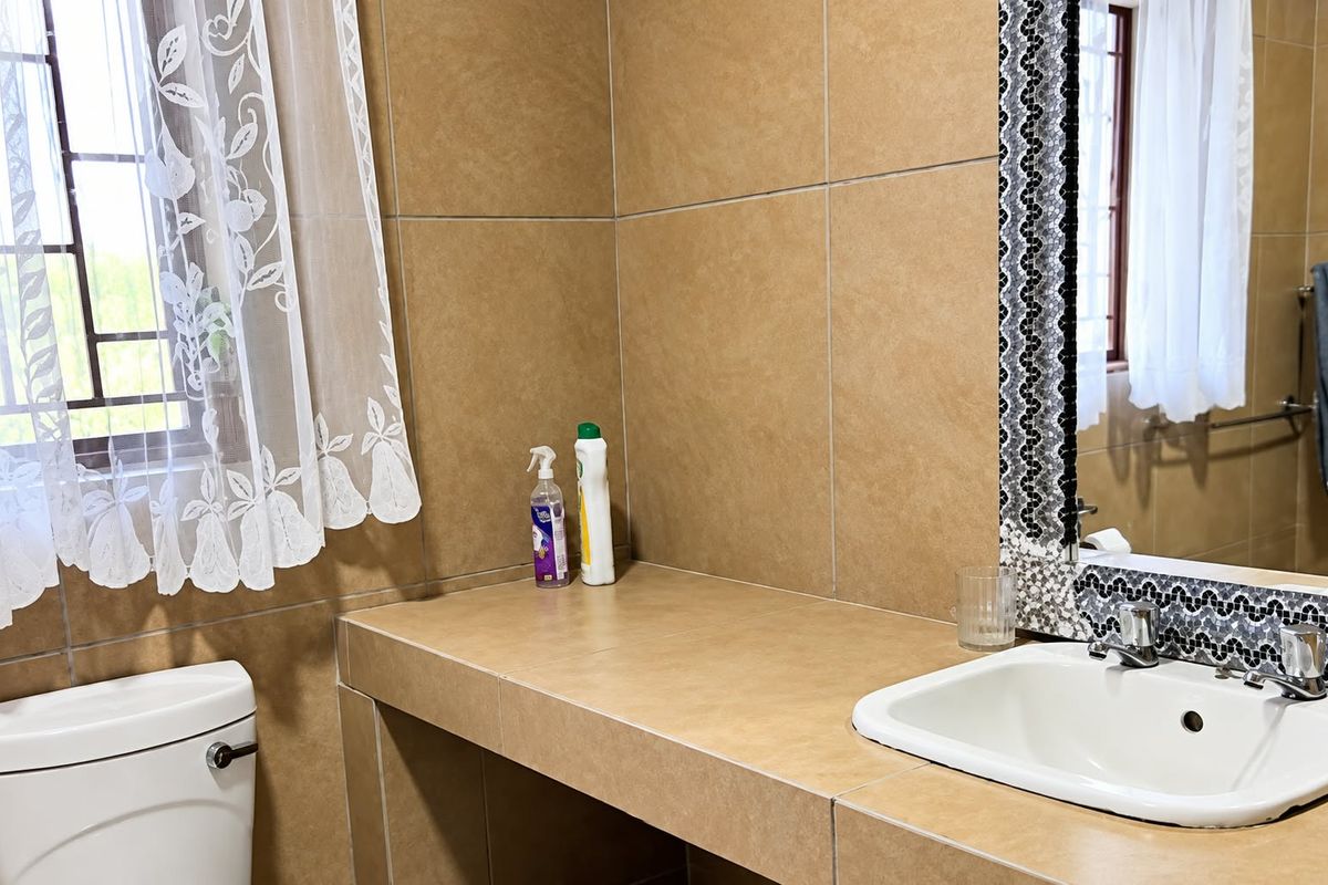 A bathroom featuring a tiled vanity countertop with a drop-in basin, chrome mixer, and decorative mosaic mirror frame, finished with neutral wall tiles.