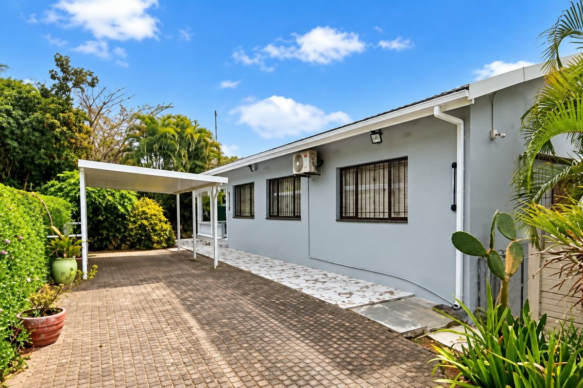 Rear exterior view of the property featuring a paved driveway, covered carport, and well-maintained exterior walls with security bars on windows.