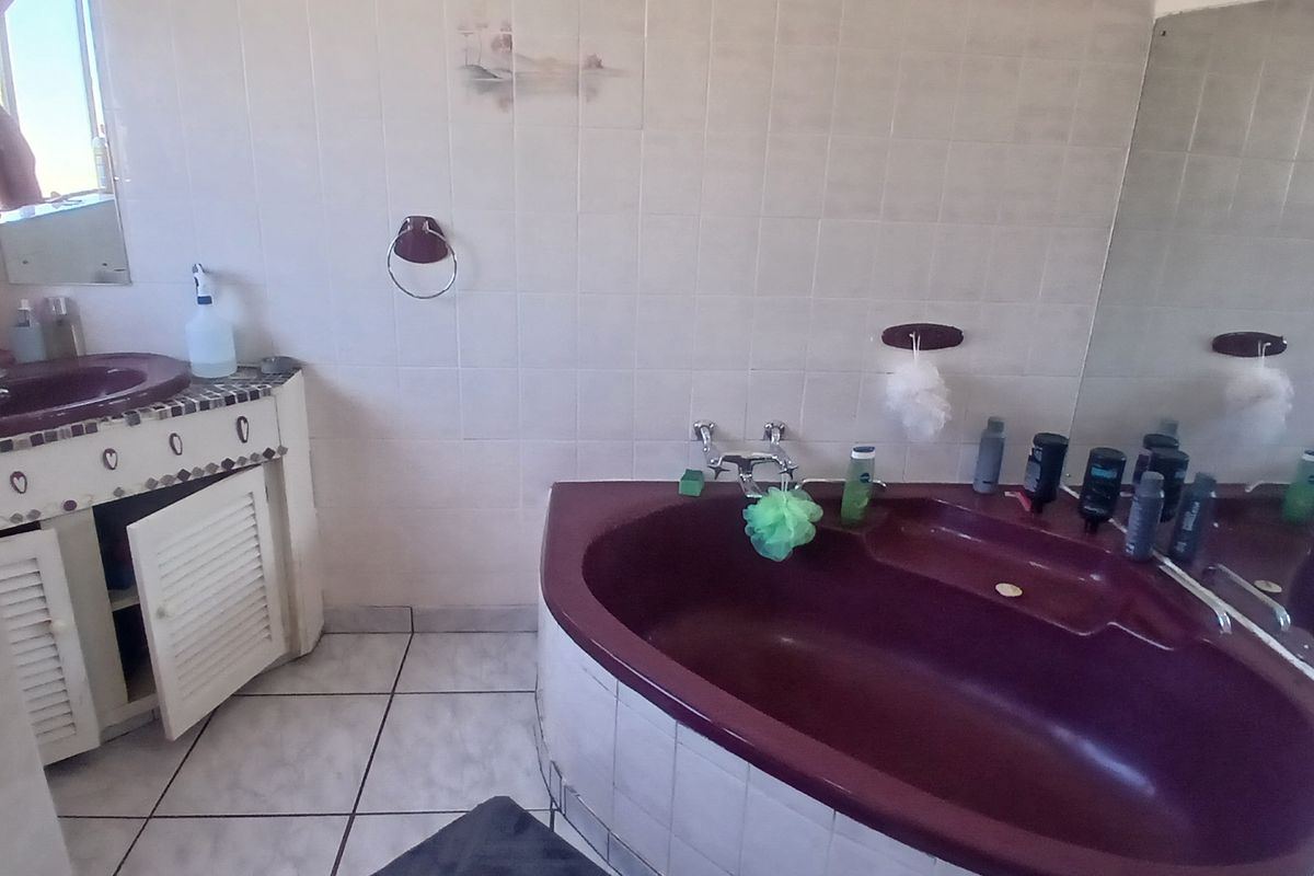 A dated bathroom featuring a corner bathtub, tiled walls and flooring, and a built-in vanity unit with a damaged cabinet door.