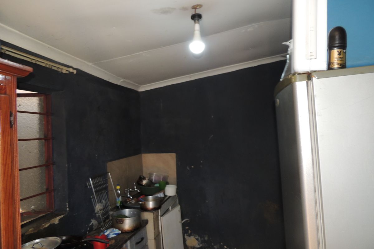 A small kitchen area featuring a sink and basic cabinetry, currently showing significant wear and tear on the wall surfaces and ceiling.