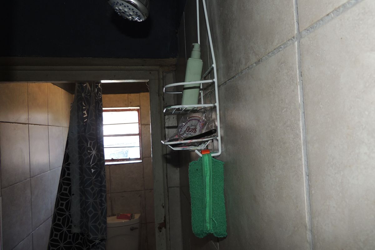 A compact bathroom featuring tiled walls, a shower head, and a toilet, showing signs of wear and dated finishes.
