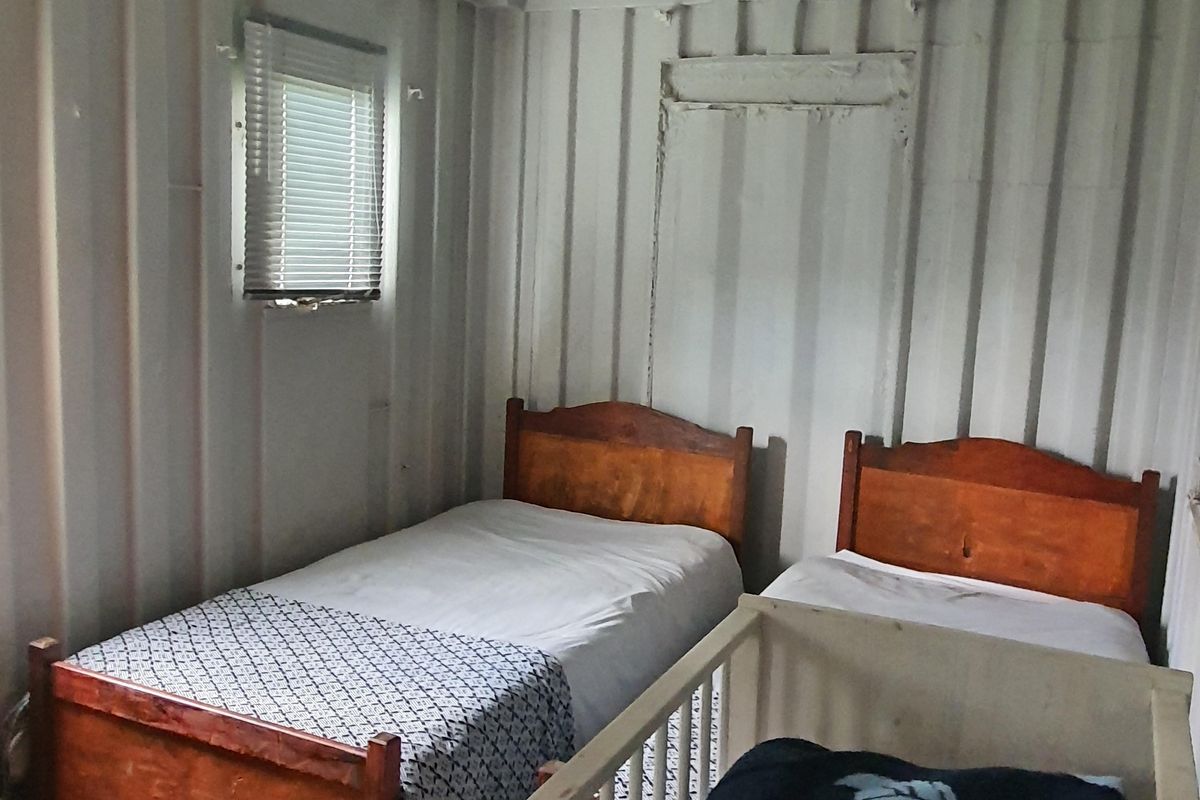 A bedroom featuring corrugated metal wall construction, laminate flooring, and a small window with fitted blinds.