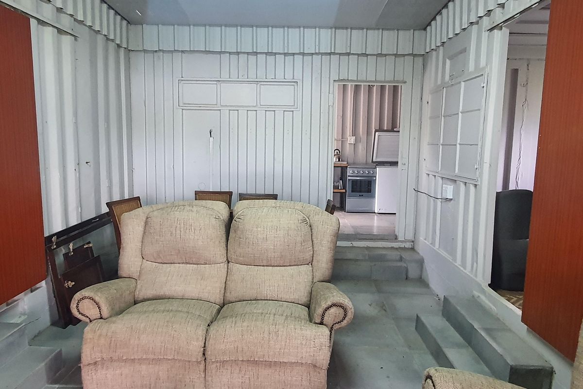 A living area featuring corrugated metal wall construction with a step-up transition leading to an adjacent kitchen space.
