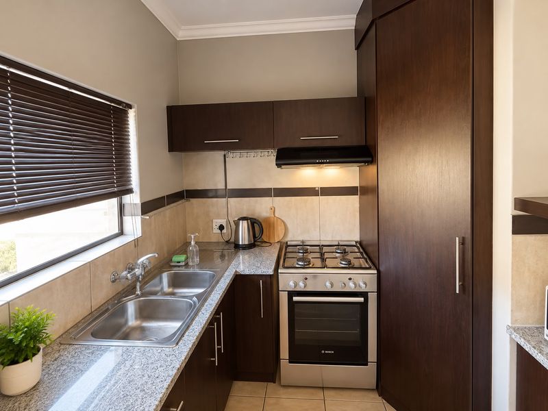 Compact, well-maintained kitchen featuring granite countertops, dark wood cabinetry, a gas hob with extractor fan, and a double bowl stainless steel sink.