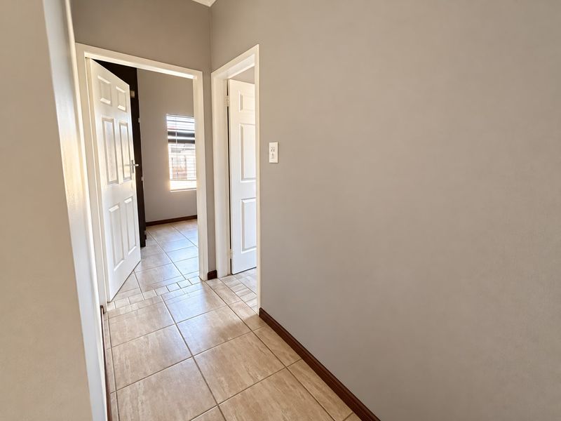 A clean and well-maintained hallway featuring neutral wall tones, tiled flooring, and access to adjacent rooms through classic panel doors.