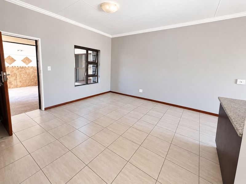A bright and spacious open-plan living area featuring neutral tiled flooring, clean grey walls, and a granite-topped breakfast counter.