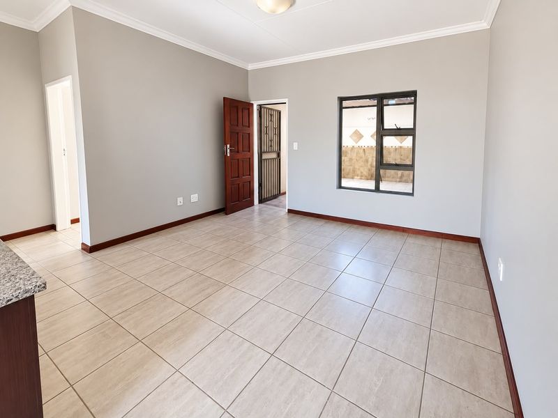 Spacious open-plan living area featuring neutral tiled flooring, clean grey walls, and a large window providing natural light.