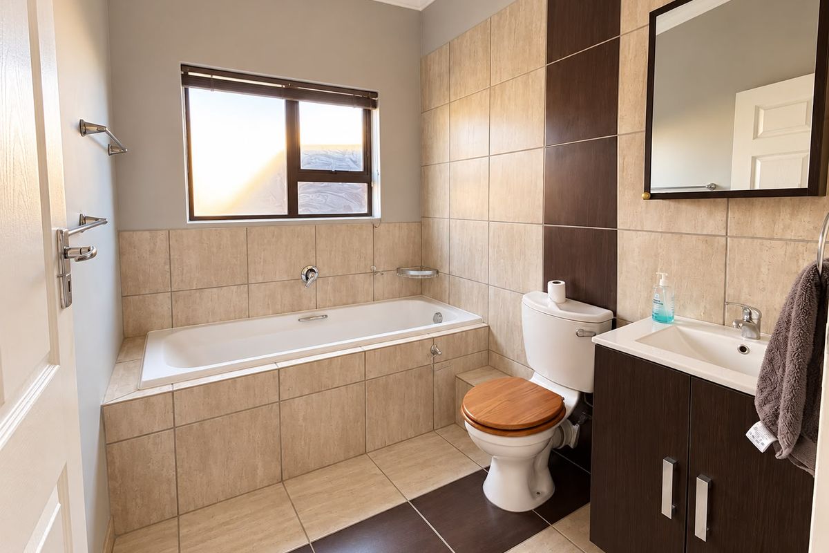 A well-maintained bathroom featuring a built-in bathtub, a modern vanity cabinet with a basin, and neutral-toned wall and floor tiling.