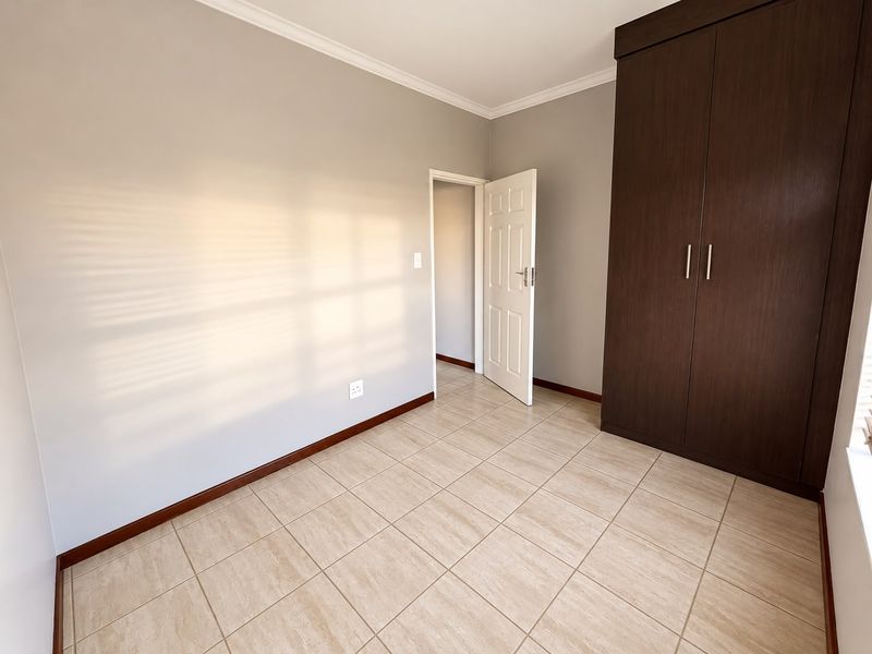 A clean, empty bedroom featuring neutral wall tones, tiled flooring, and dark wood built-in cupboards, offering a versatile space ready for personalization.