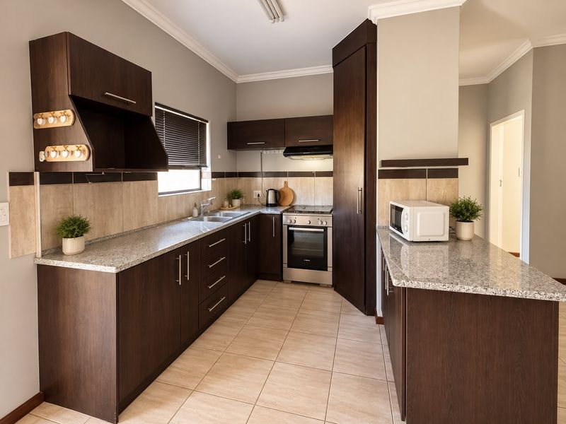 A well-maintained kitchen featuring dark wood cabinetry, granite countertops, a built-in oven with extractor fan, and neutral tiled flooring.