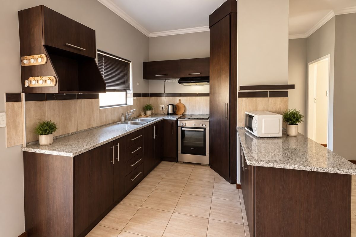 A well-maintained kitchen featuring dark wood cabinetry, granite countertops, a built-in oven with extractor fan, and neutral tiled flooring.
