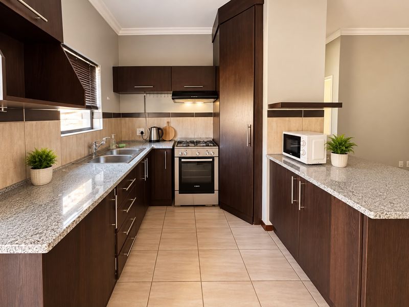 Modern kitchen featuring dark wood cabinetry, granite countertops, stainless steel gas stove, oven, extractor fan, and tiled flooring.