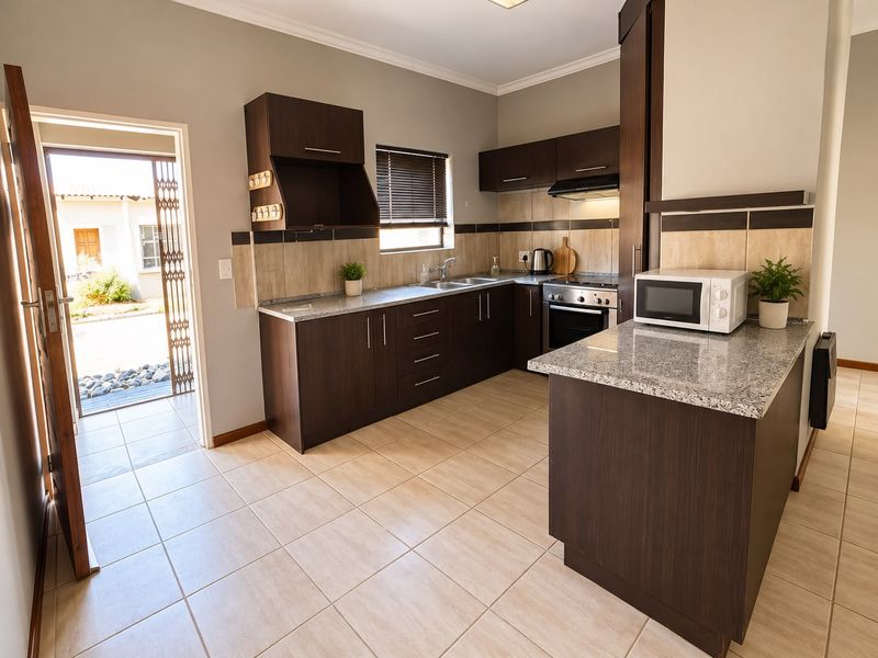 A functional kitchen featuring dark wood cabinetry, granite countertops, tiled flooring, and direct access to an outdoor area through a security gate.