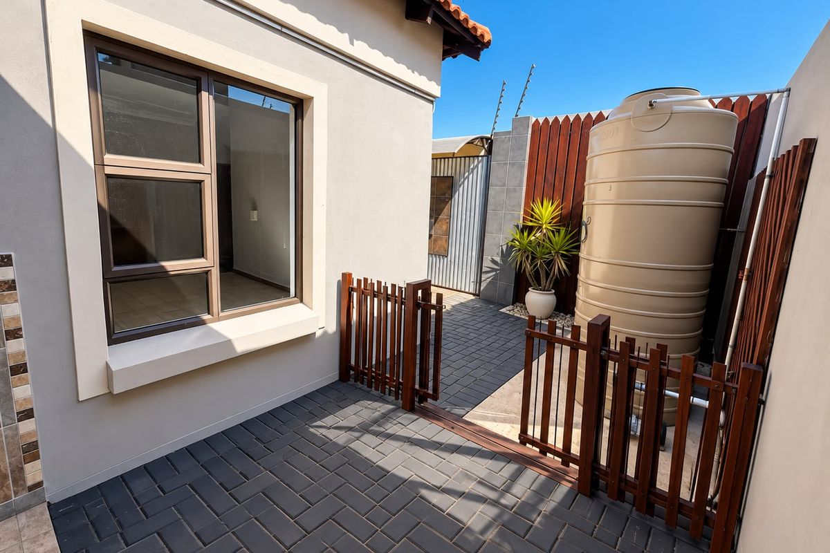 A well-maintained rear courtyard featuring paved flooring, a water storage tank, and secure timber fencing with integrated electric security wires.